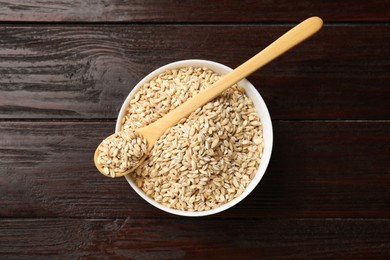 Photo of Dry pearl barley in bowl and spoon on wooden table, top view