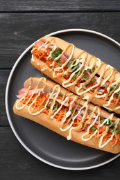 Delicious hot dogs with bacon, carrot and parsley on black wooden table, top view