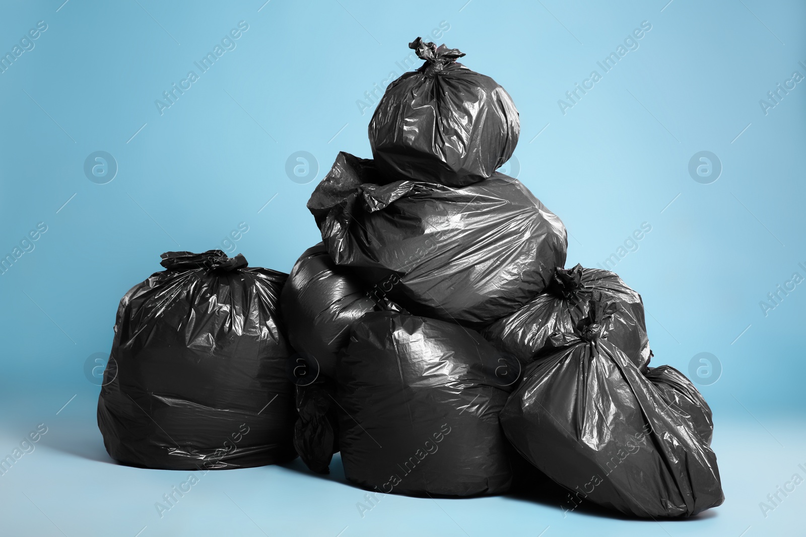 Photo of Black trash bags full of garbage on light blue background