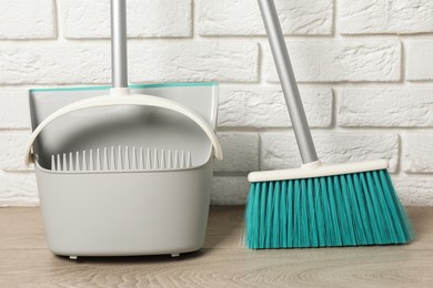 Photo of Plastic broom with dustpan near white brick wall indoors