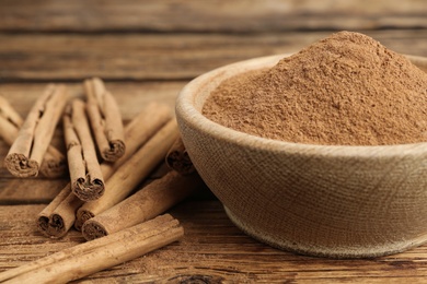 Aromatic cinnamon powder in bowl and sticks on wooden table, closeup