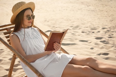 Young woman reading book in deck chair on sandy beach