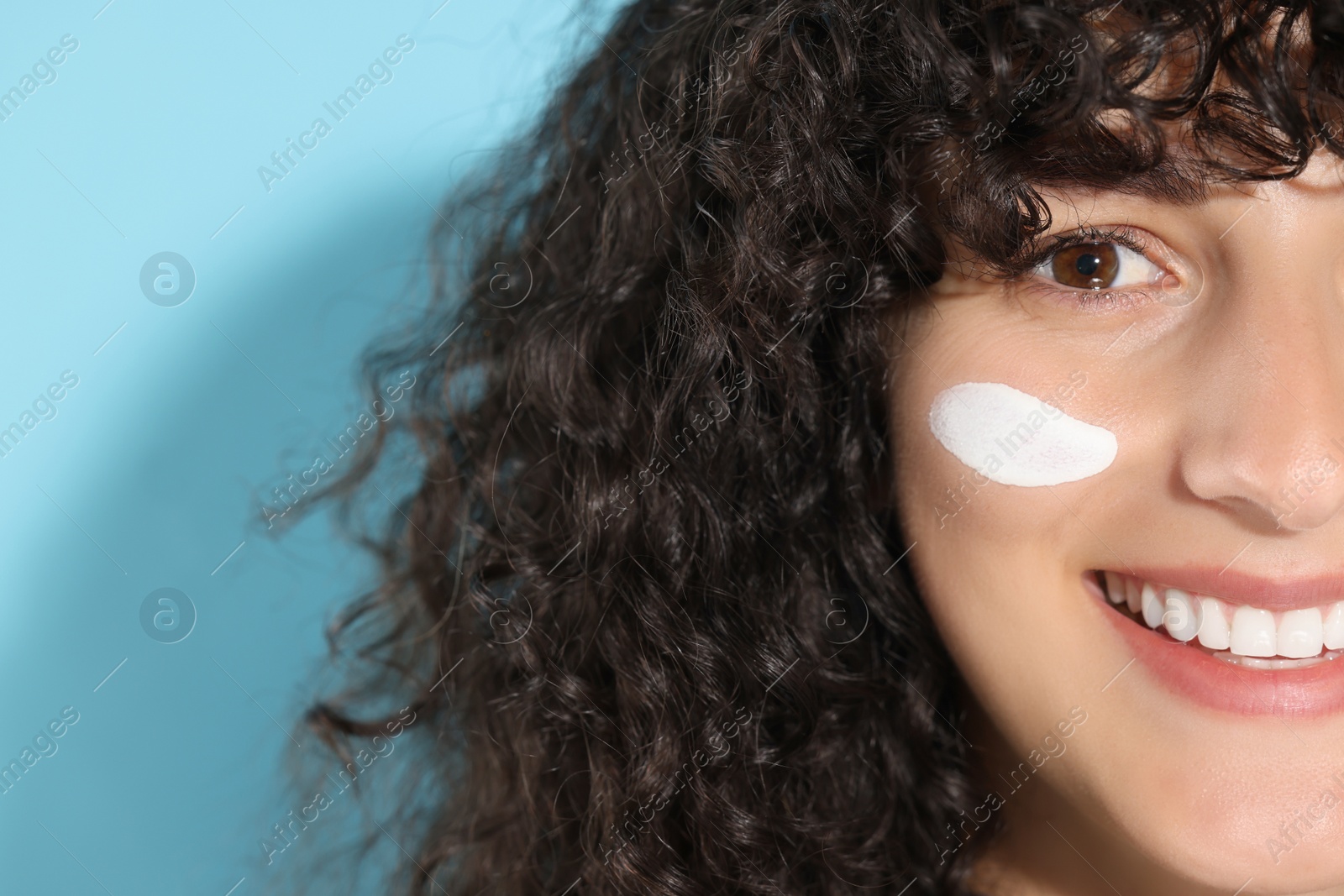 Photo of Beautiful young woman with sun protection cream on her face against light blue background, closeup. Space for text