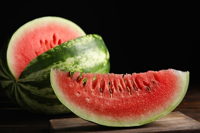 Photo of Yummy watermelon on wooden table against black background