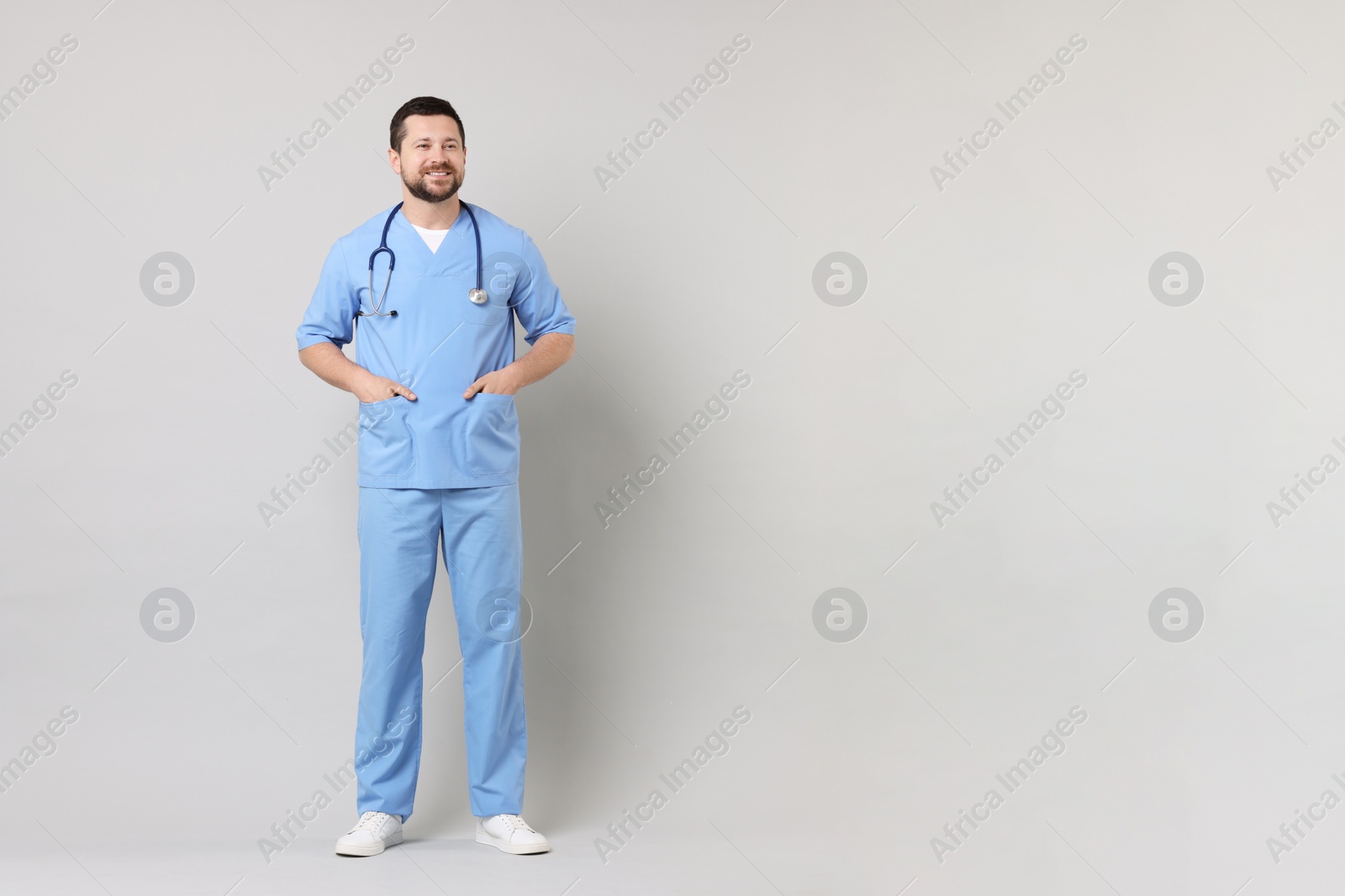 Photo of Full length portrait of smiling doctor on light grey background. Space for text