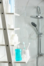 Bottle of mouthwash, toothbrushes and dental floss on white shelf in bathroom