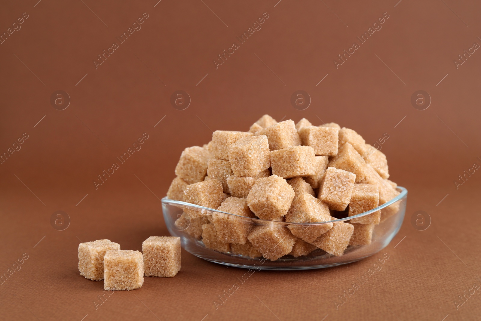 Photo of Brown sugar cubes in bowl on color background, closeup