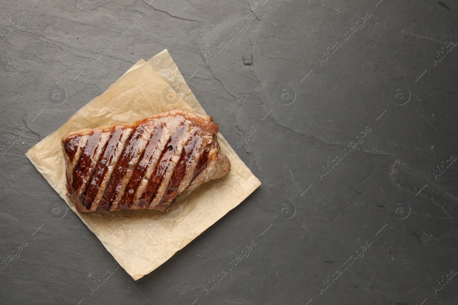 Photo of Delicious grilled beef steak on dark gray table, top view. Space for text