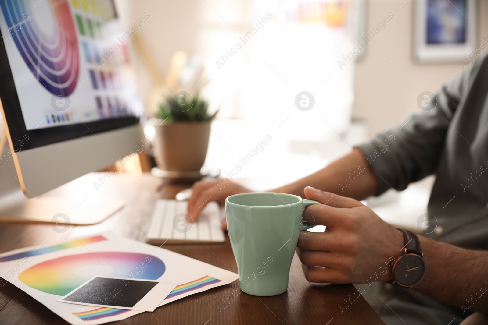 Photo of Designer with cup of drink working at table in office, closeup