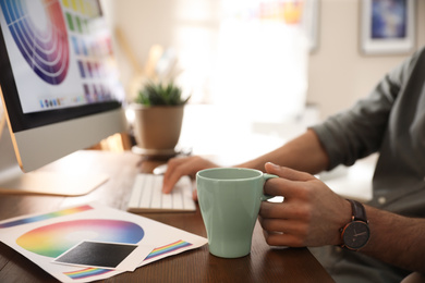 Designer with cup of drink working at table in office, closeup