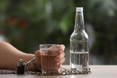 Man chained to glass of vodka at table against blurred background, closeup. Alcohol addiction