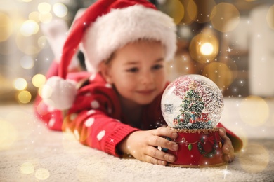 Image of Little girl in Santa hat playing with snow globe on floor. Bokeh effect