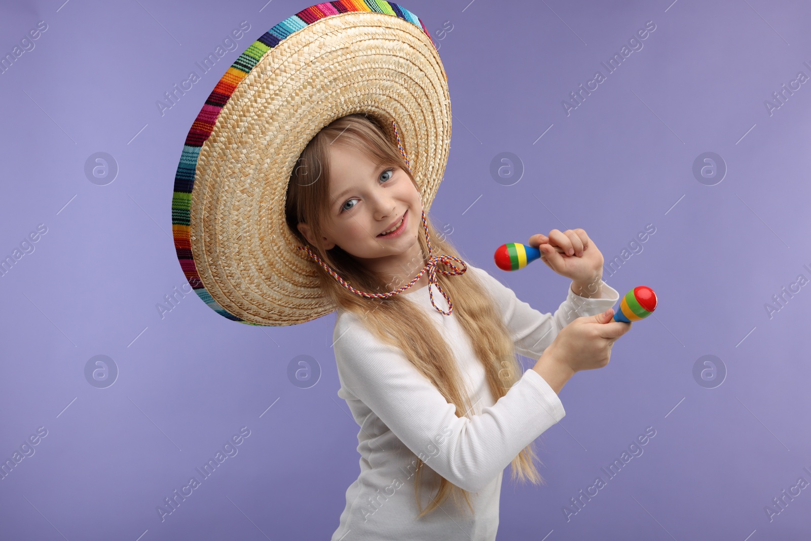 Photo of Cute girl in Mexican sombrero hat dancing with maracas on purple background