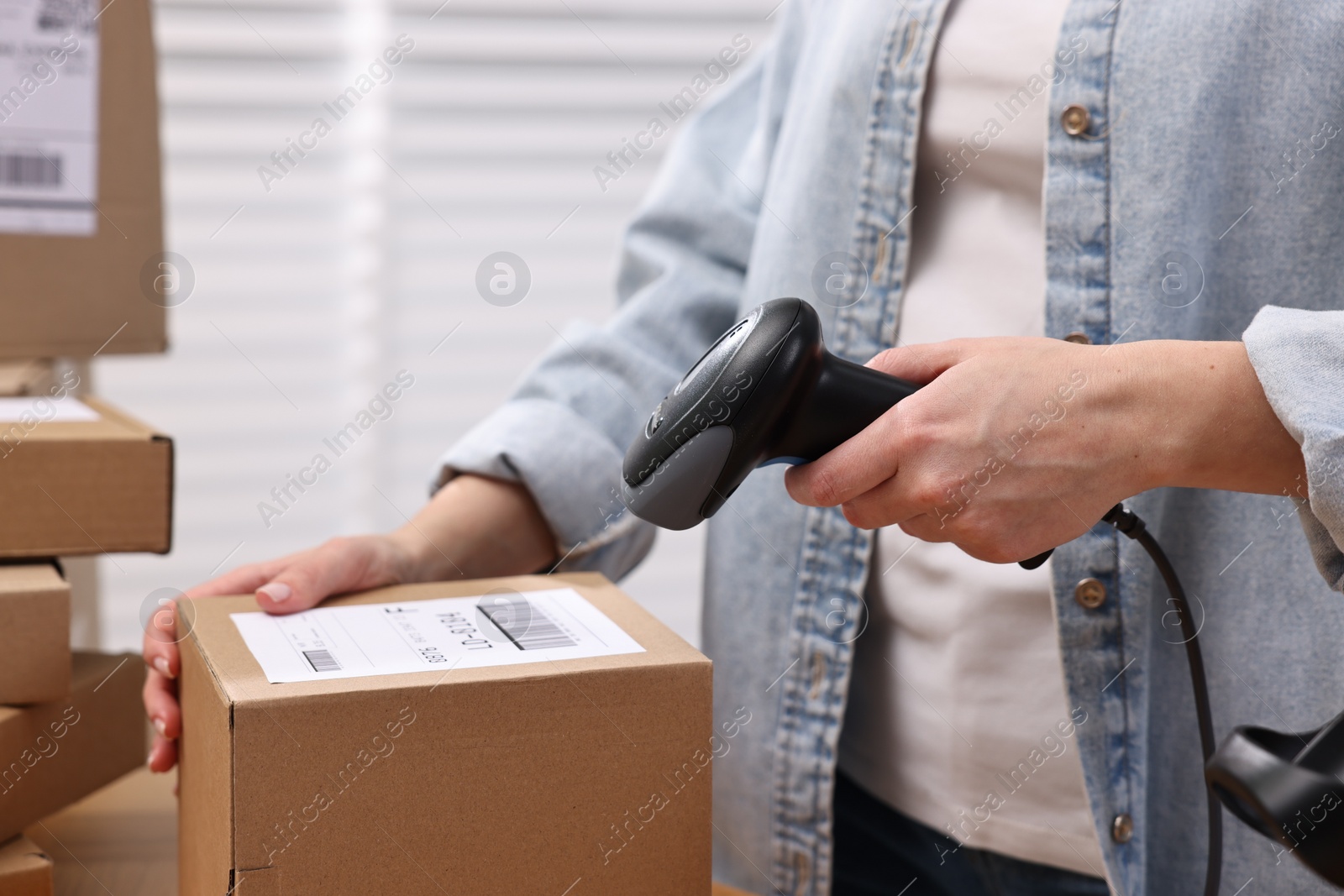 Photo of Parcel packing. Post office worker with scanner reading barcode indoors, closeup