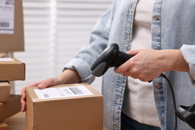 Photo of Parcel packing. Post office worker with scanner reading barcode indoors, closeup