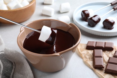 Photo of Dipping marshmallow into melted chocolate on light grey marble table