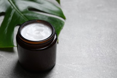 Photo of Jar of hand cream and green leaf on grey table, space for text