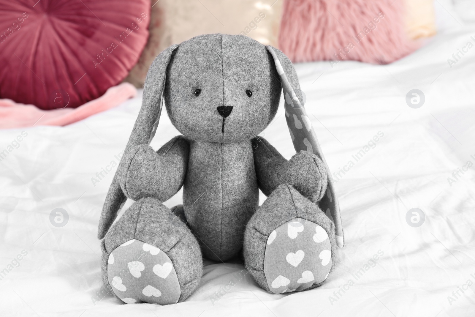 Photo of Cute stuffed toy rabbit on comfortable bed in child's room interior