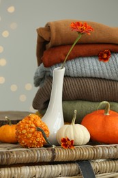 Photo of Beautiful autumn flowers, pumpkins and stacked clothes on wicker table