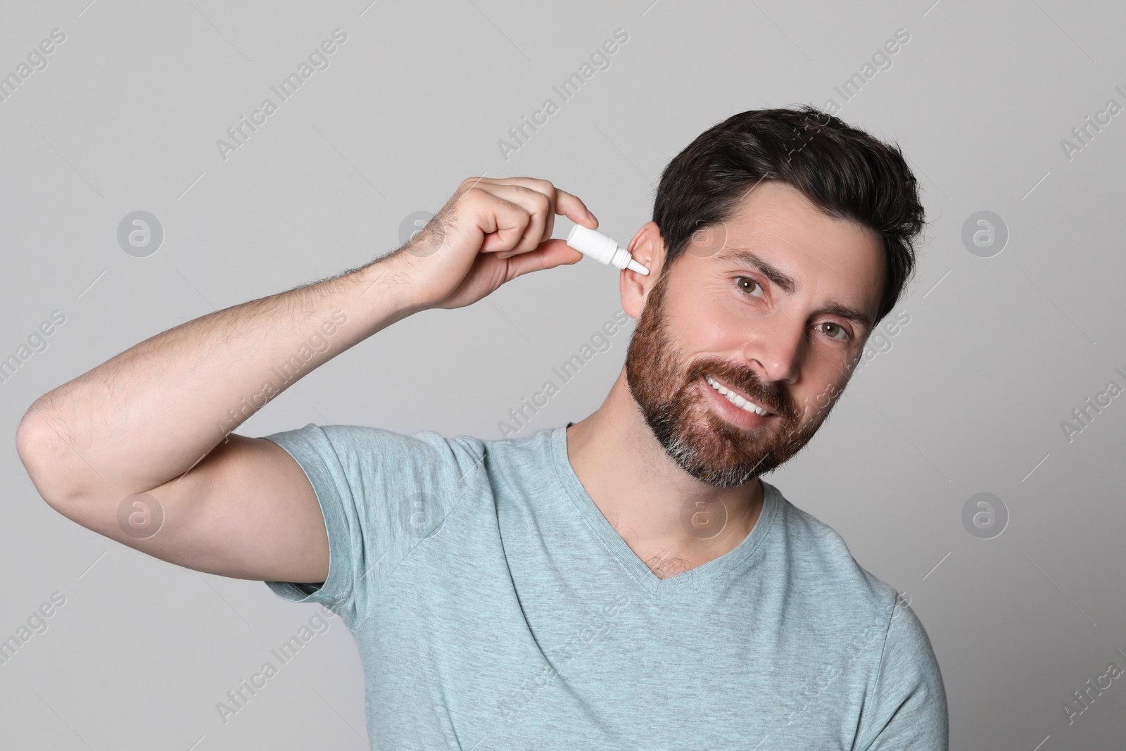 Photo of Man using ear drops on grey background