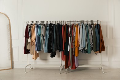 Photo of Racks with stylish clothes and mirror near white wall indoors. Fast fashion