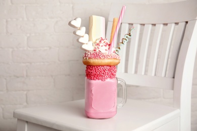 Photo of Tasty milk shake with sweets in mason jar on chair near brick wall