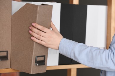 Photo of Woman taking folder with documents from shelf in office, closeup