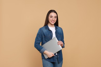 Smiling young woman with laptop on beige background