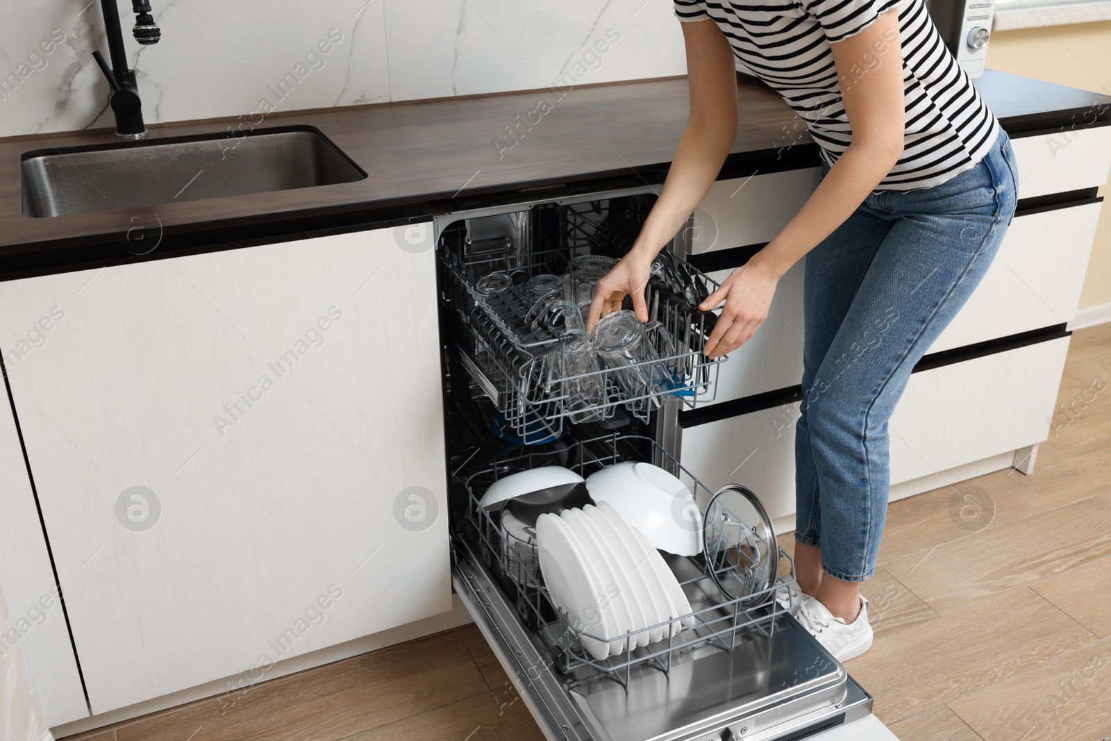 Photo of Woman loading dishwasher with glasses and plates in kitchen, closeup