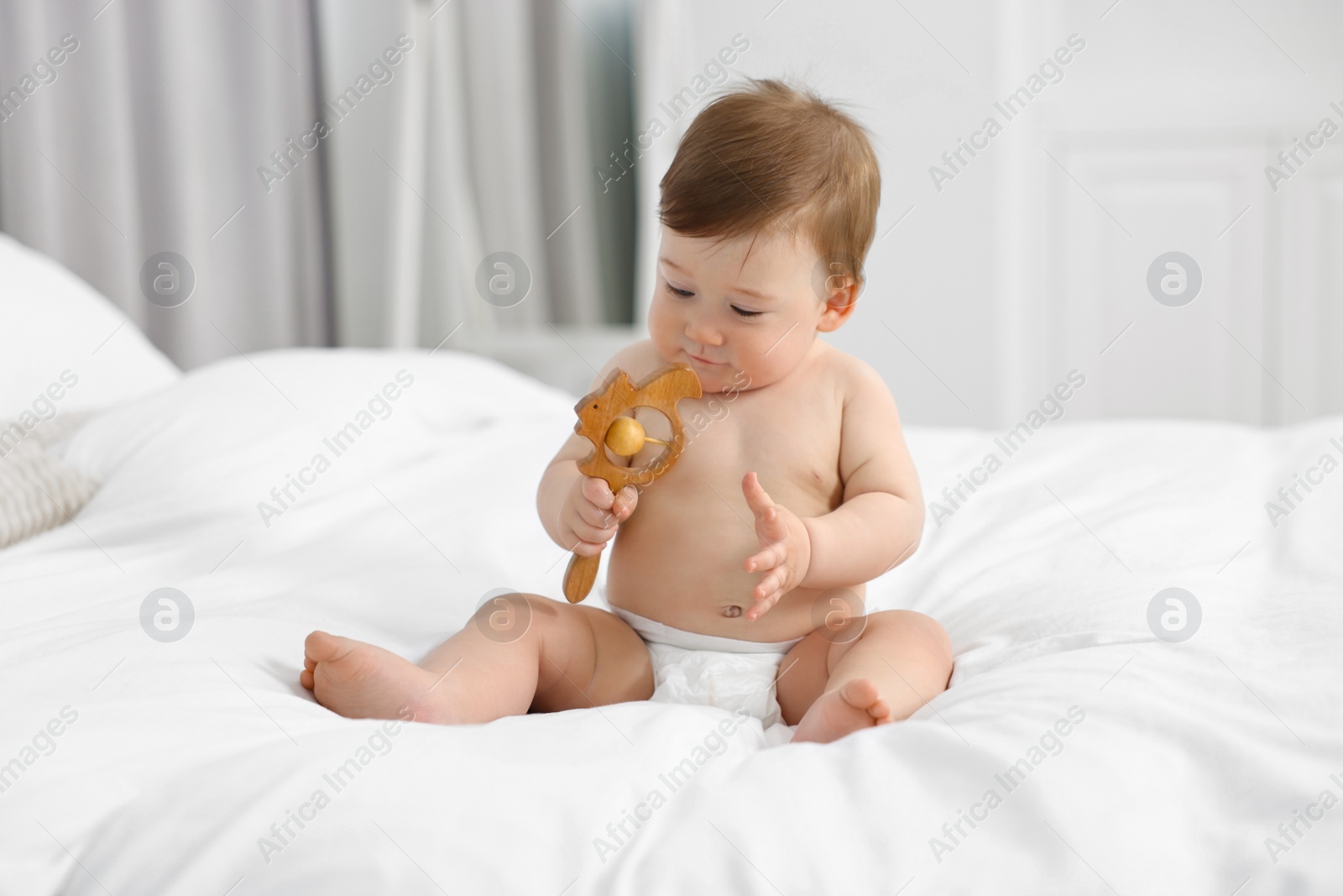 Photo of Cute baby boy with wooden rattle on bed at home