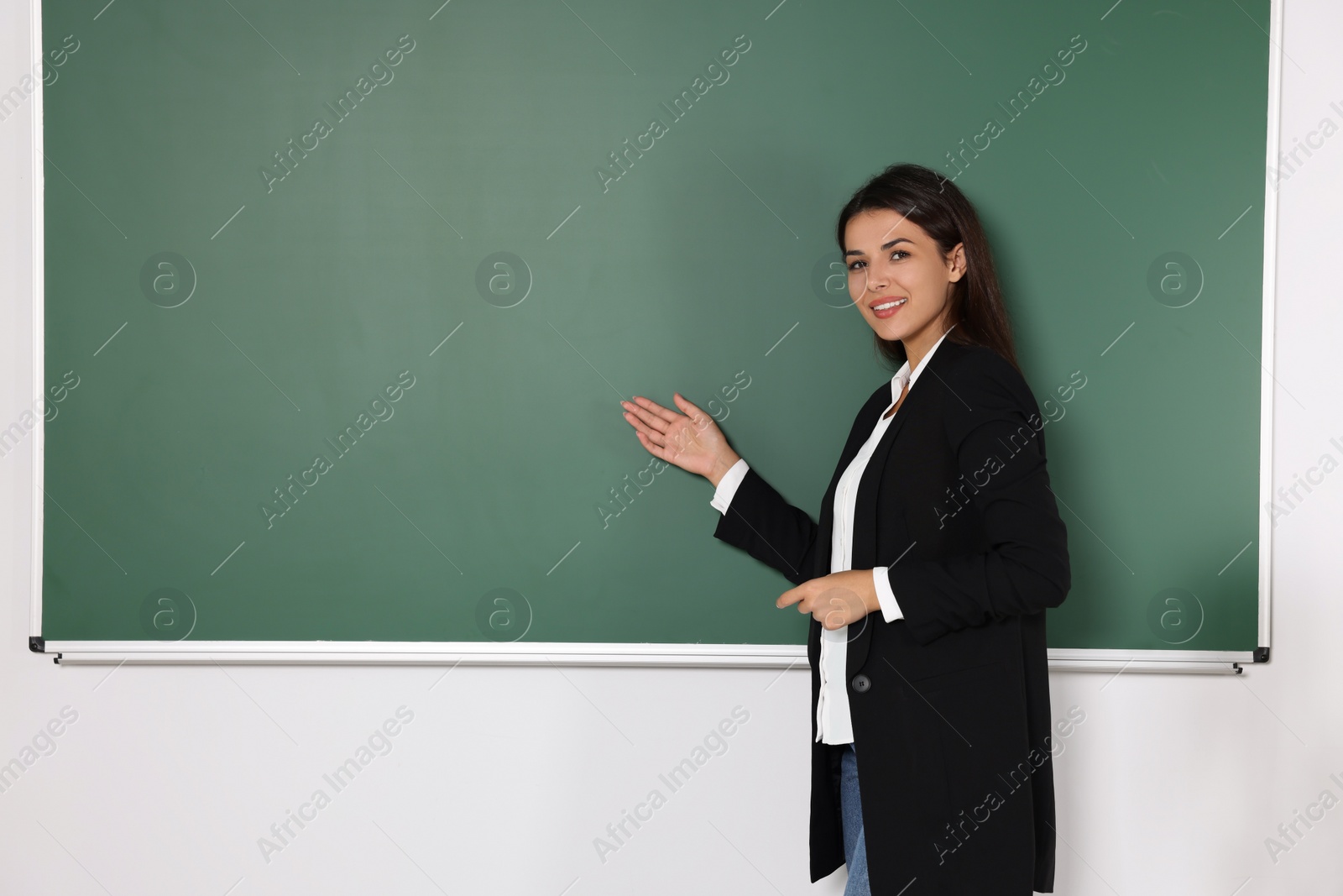 Photo of Happy young teacher giving lesson at blackboard in classroom. Space for text