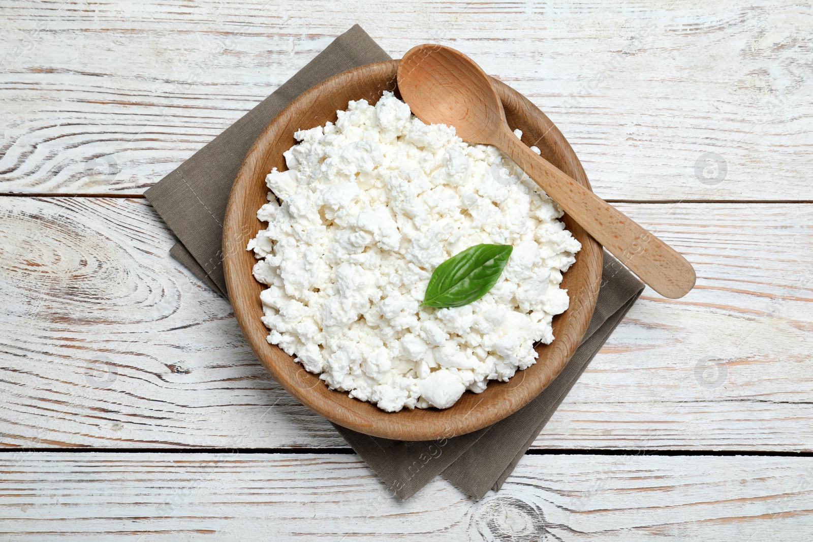 Photo of Delicious cottage cheese with basil on white wooden table, top view