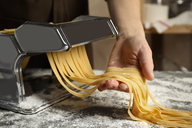 Woman preparing noodles with pasta maker machine at table indoors, closeup