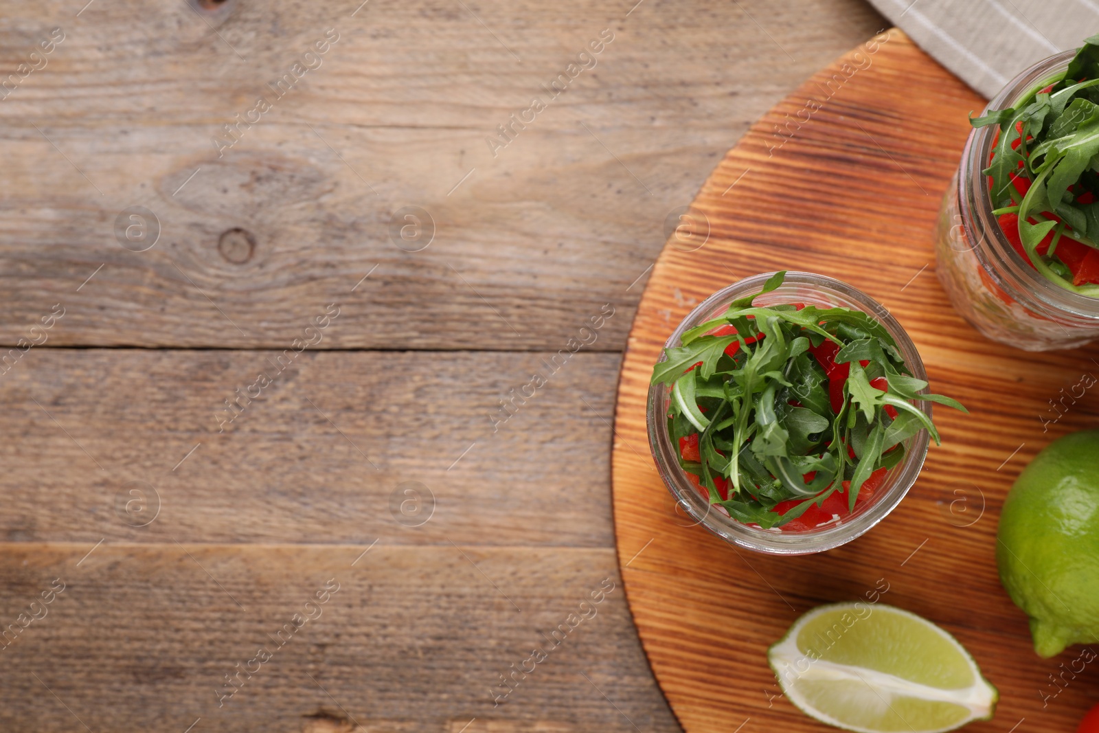 Photo of Healthy salad in glass jars on wooden table, flat lay. Space for text