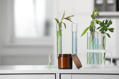 Photo of Glass tubes with leaves and jar of cream on white lab drawer indoors, space for text