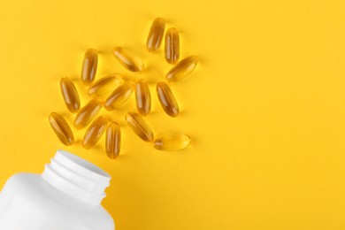 Photo of White medical bottle and vitamin capsules on yellow background, top view. Space for text