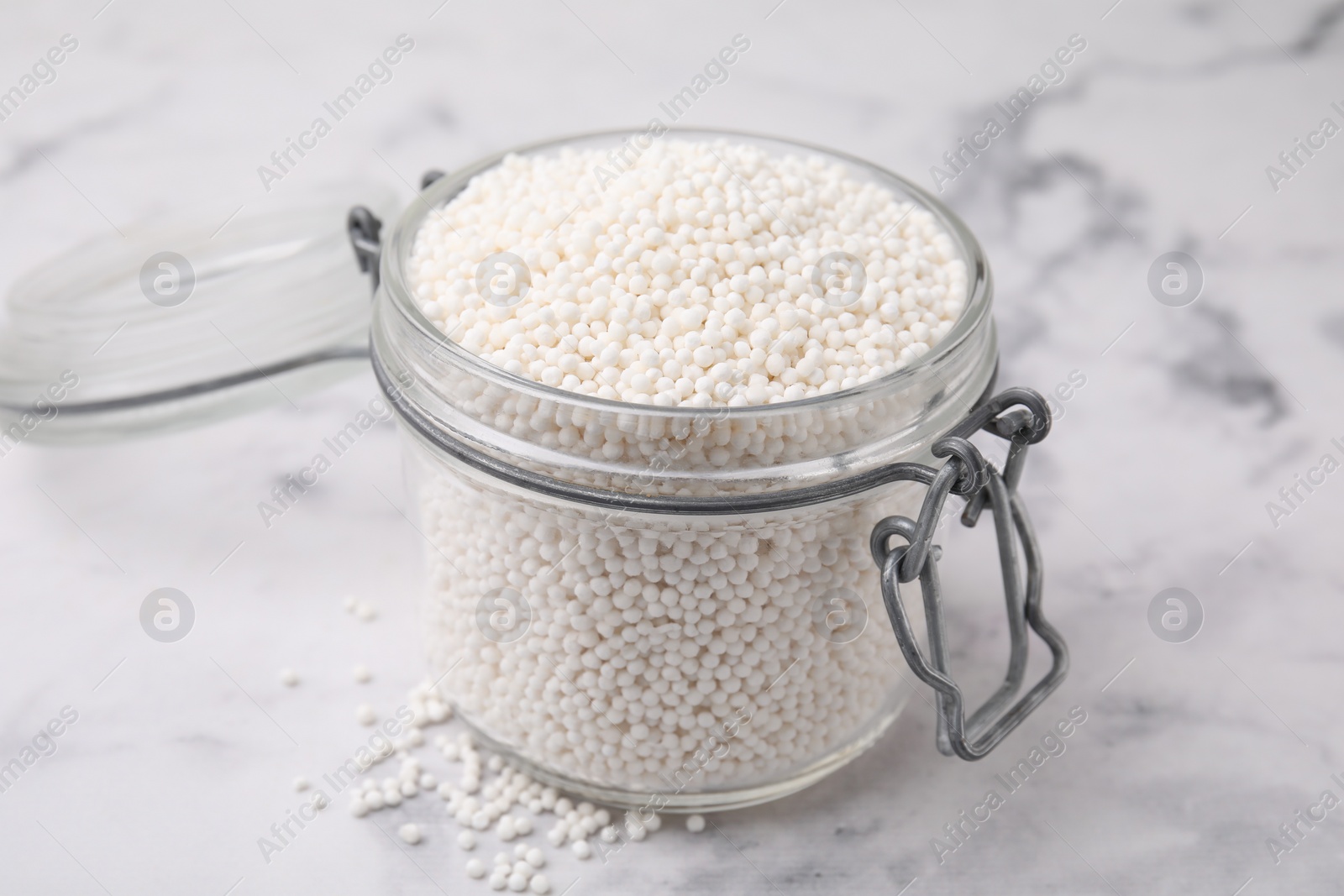 Photo of Tapioca pearls in jar on white marble table, closeup