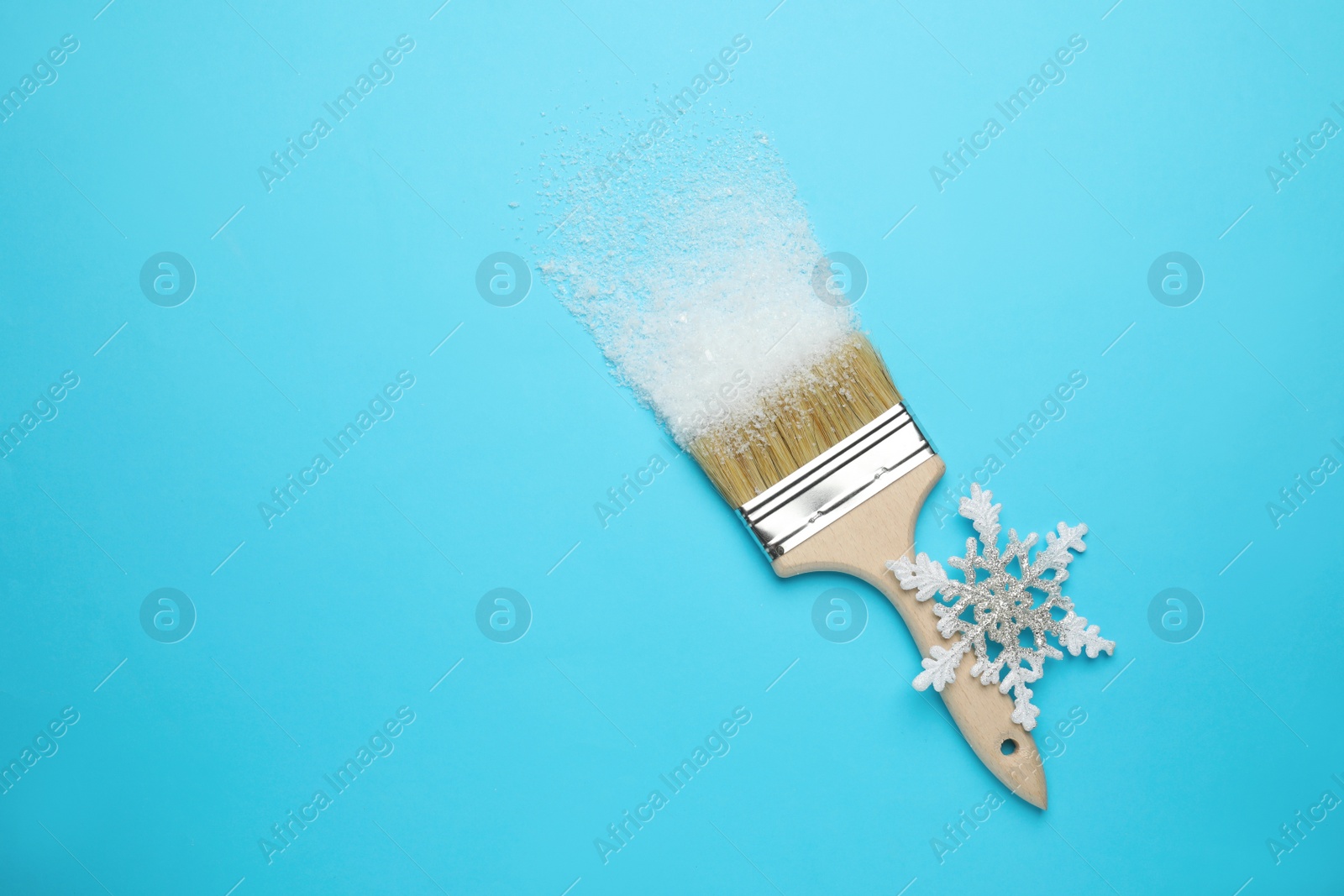 Photo of Brush painting with artificial snow on light blue background, top view. Space for text. Creative concept