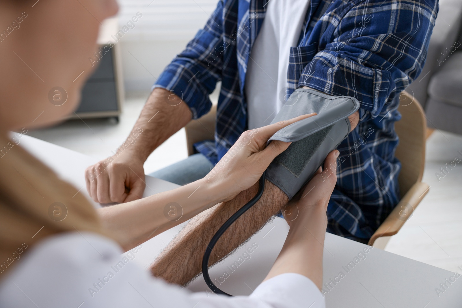 Photo of Doctor measuring blood pressure of man at table indoors, closeup