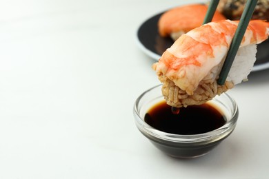 Photo of Dipping tasty sushi into soy sauce at white table, closeup. Space for text