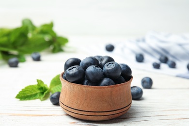 Wooden bowl with tasty blueberries on white table