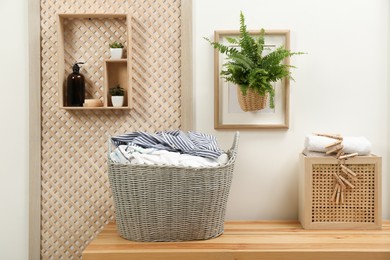 Wicker basket with dirty laundry on wooden table in bathroom