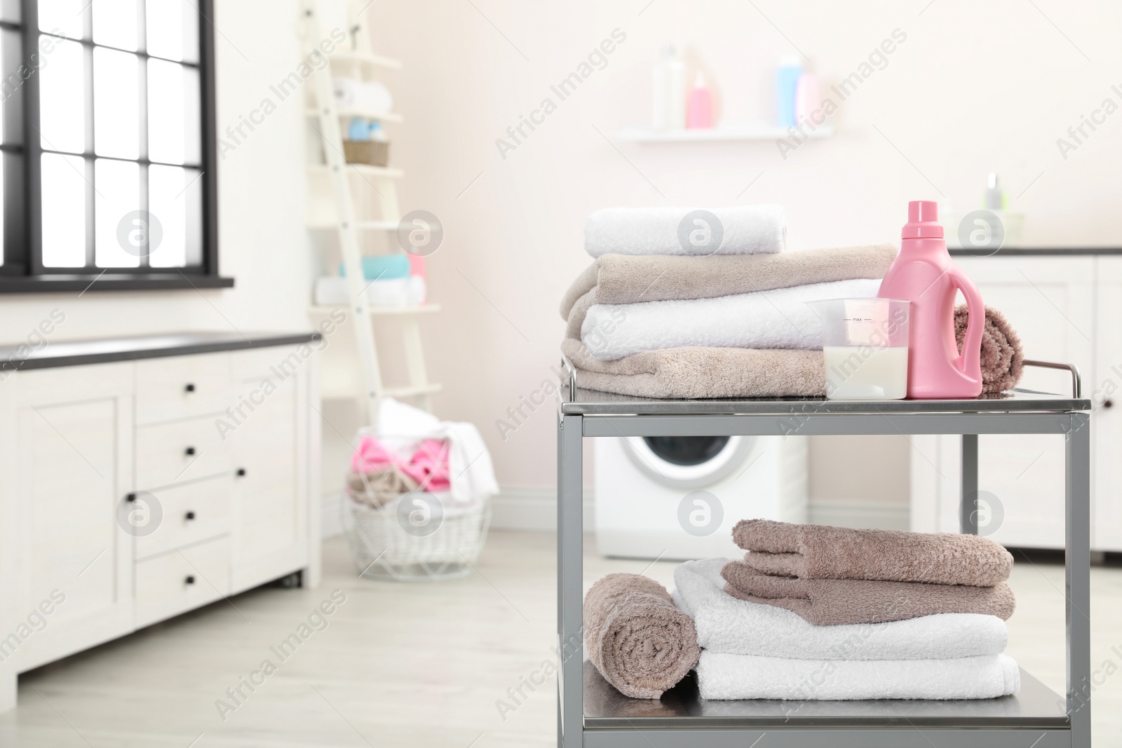 Photo of Soft bath towels and detergent on metal cart against blurred background, space for text