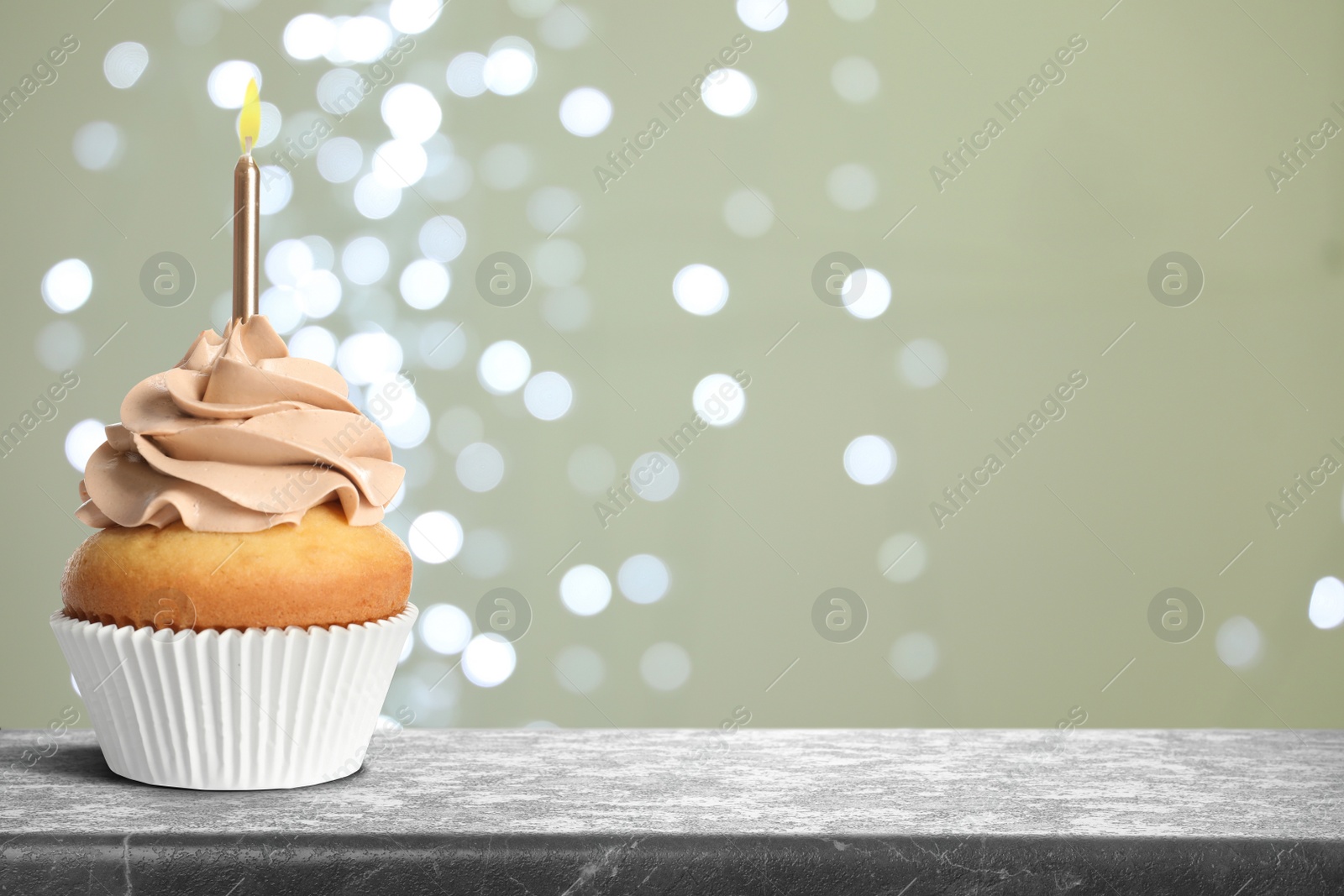 Image of Tasty birthday cupcake with candle on grey table against blurred lights. Space for text