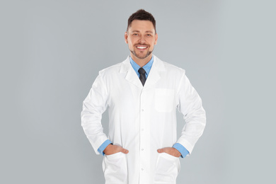 Happy man in lab coat on light grey background