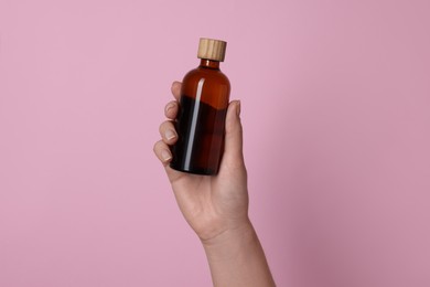 Photo of Woman holding bottle of cosmetic product on pink background, closeup