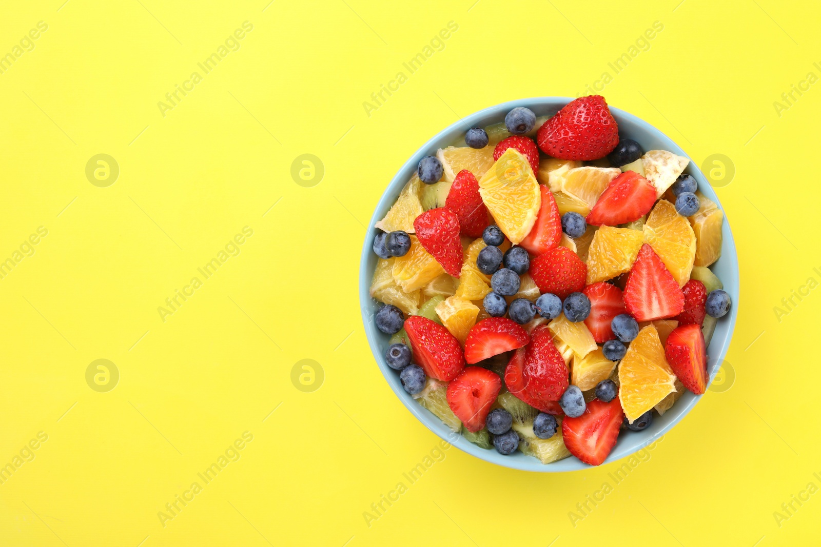Photo of Yummy fruit salad in bowl on yellow background, top view. Space for text