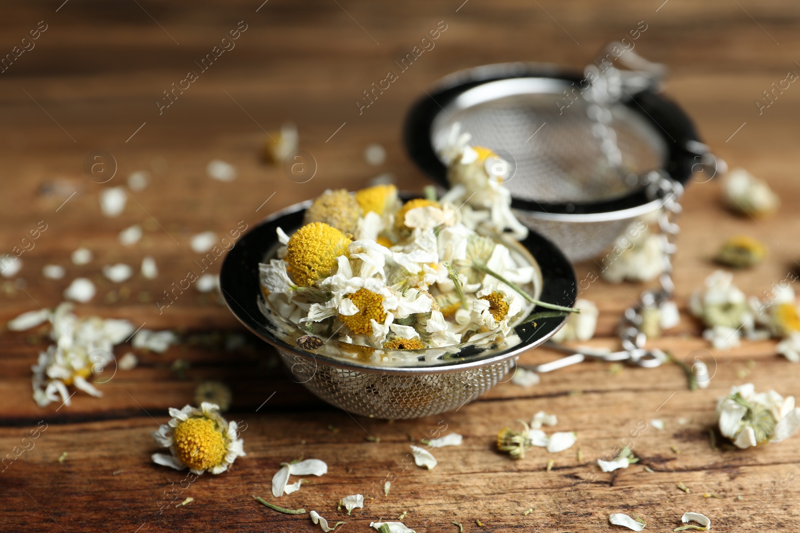 Photo of Dry chamomile flowers in infuser on wooden table, closeup