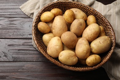 Photo of Raw fresh potatoes in wicker basket on wooden table, top view. Space for text