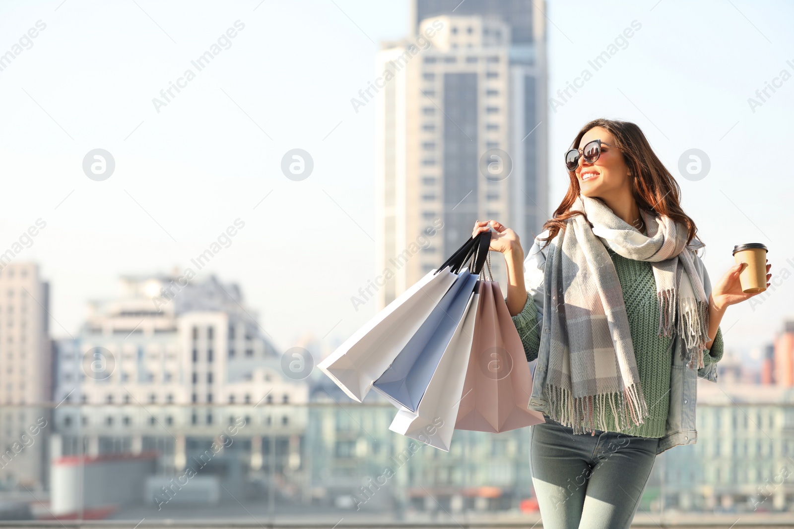 Photo of Beautiful young woman with cup of coffee and shopping bags on city street